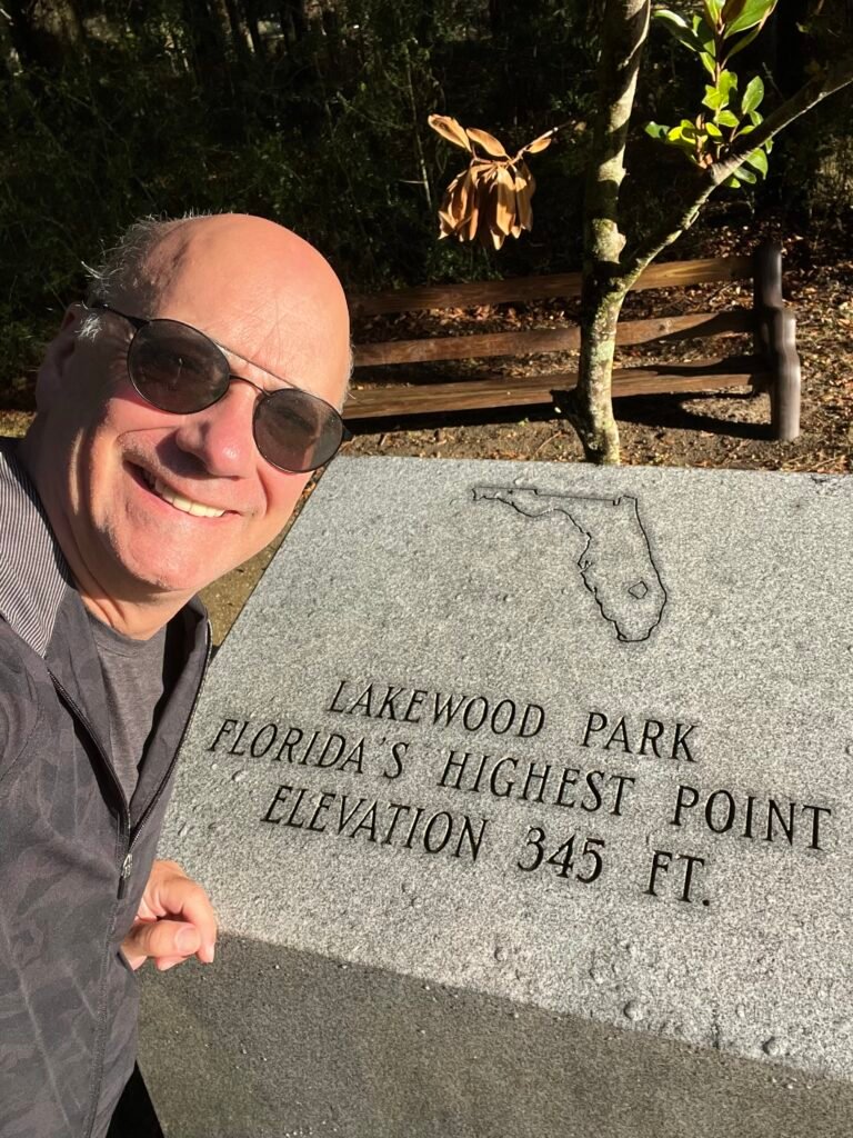 Smiling hiker at the Britton Hill high point marker in Lakewood Park, Florida’s highest point at 345 feet