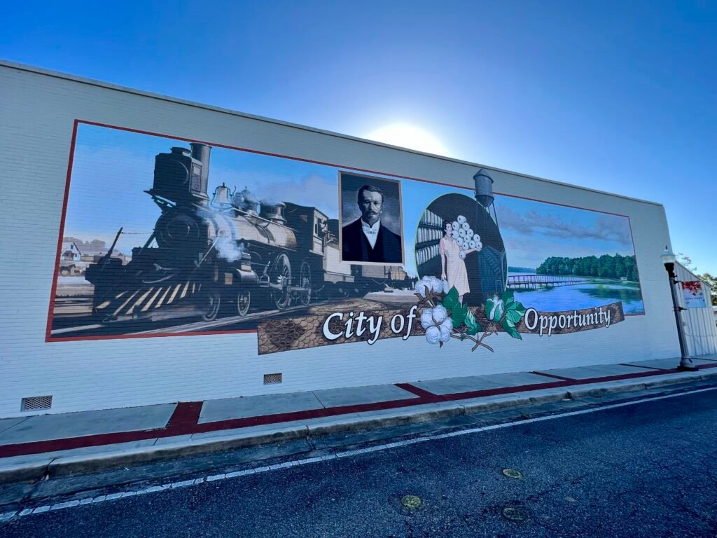 Mural in Opp, Alabama reading “City of Opportunity,” featuring a steam locomotive, cotton, and a historic portrait on a downtown building.