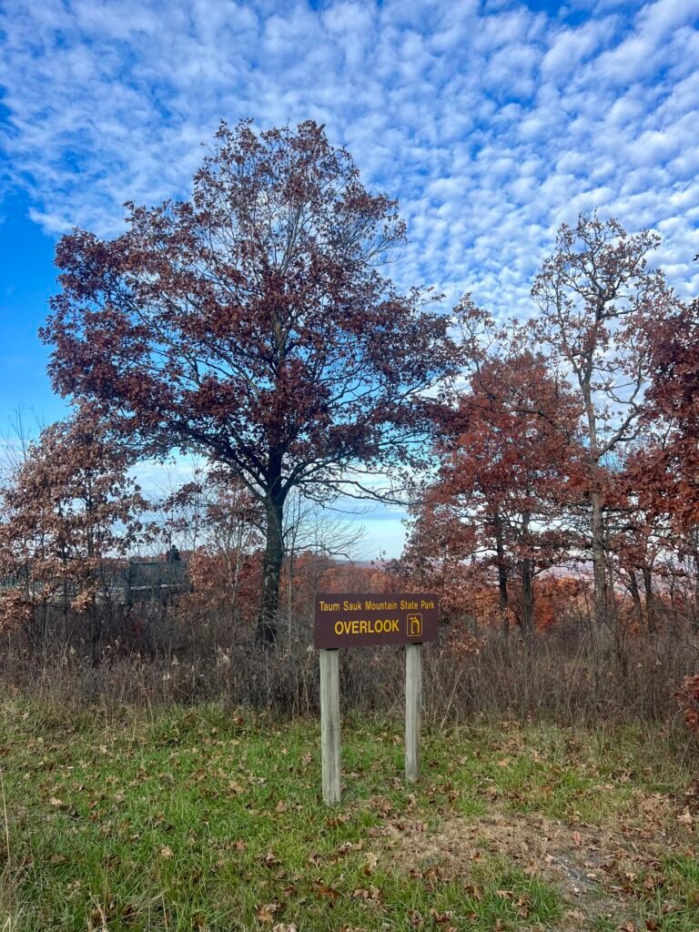 Taum Sauk Mountain State Park Overlook sign with autumn trees and scenic Ozark views under a blue sky.