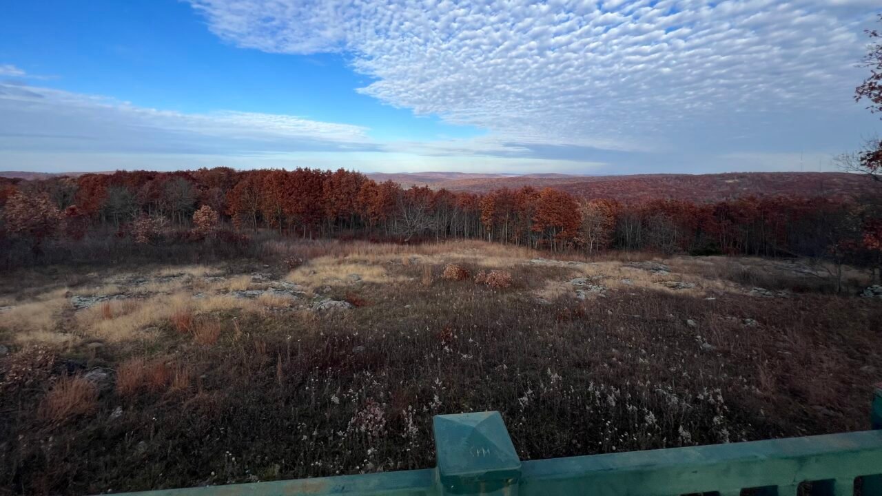 Panoramic view from Taum Sauk Mountain Overlook showing rolling Ozark hills and fall foliage beneath dramatic textured clouds.