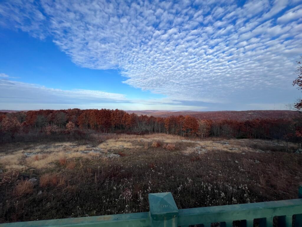 Panoramic view from Taum Sauk Mountain Overlook showing rolling Ozark hills and fall foliage beneath dramatic textured clouds.