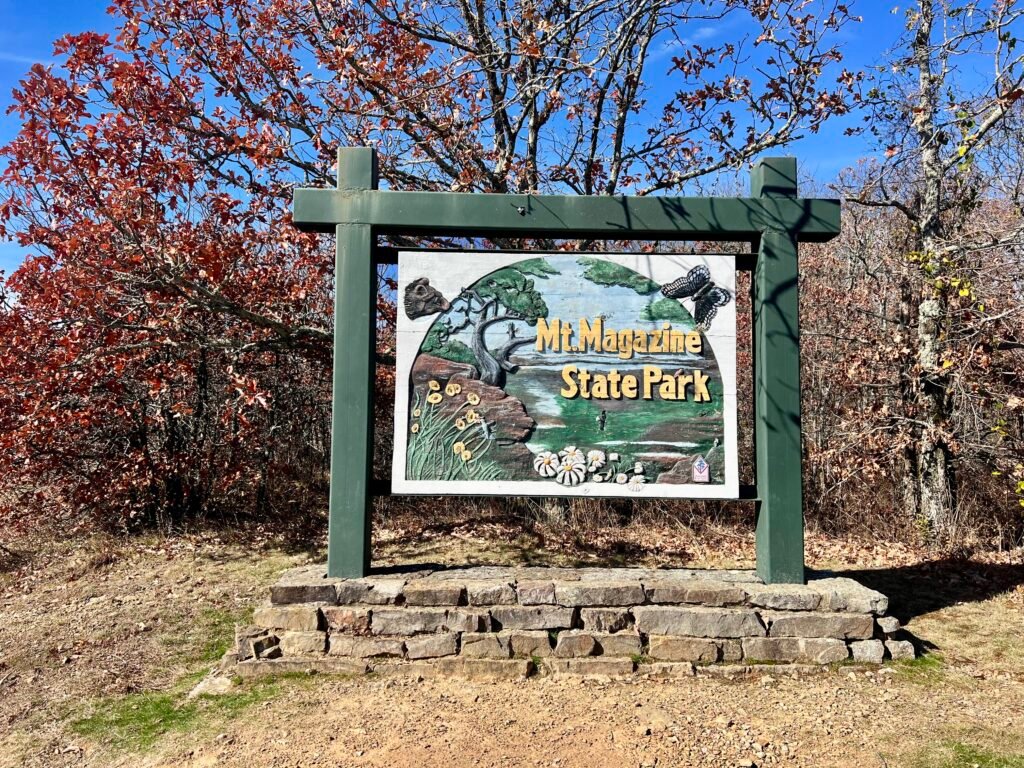 Mount Magazine State Park entrance sign in Arkansas with autumn trees and blue sky.