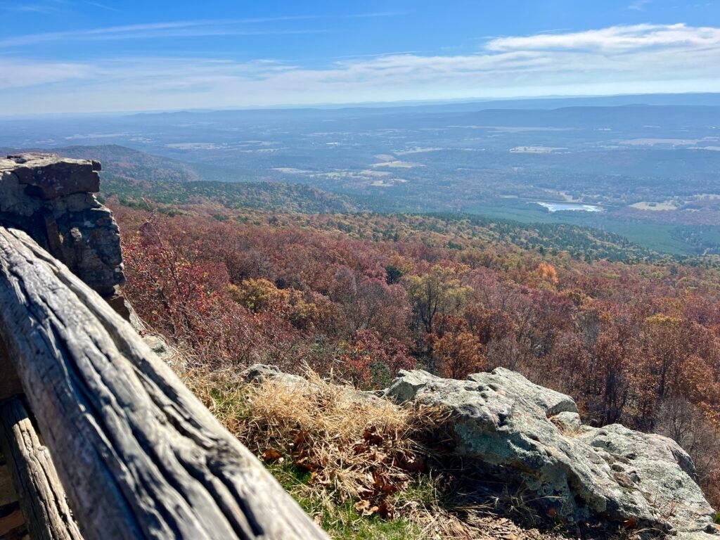 Panoramic fall view from Petit Jean Valley Overlook at Mount Magazine State Park with colorful forest and distant mountains.