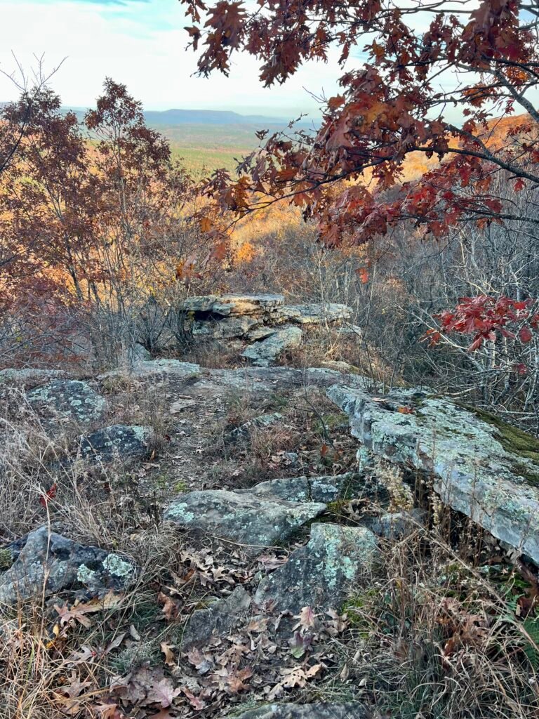 Rocky overlook at Sunrise Rock framed by fall foliage with distant Arkansas hills beyond.