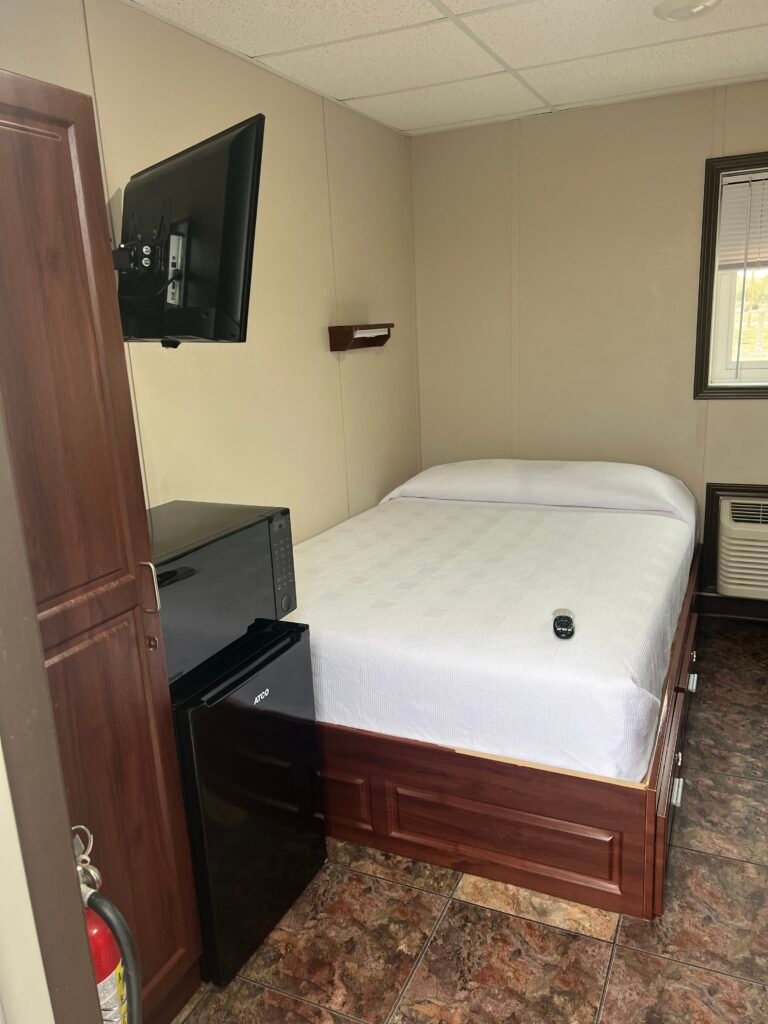 Simple hotel room at Karbani Inn with bed, mini fridge, microwave, and wall-mounted TV.
