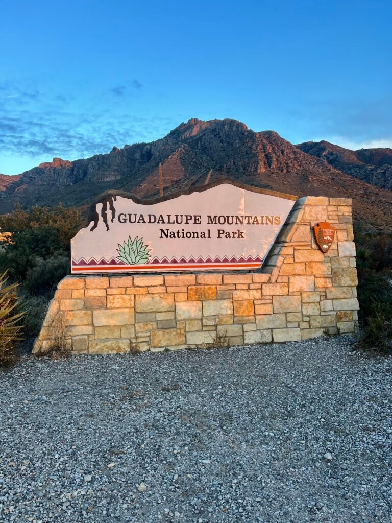 Guadalupe Mountains National Park entrance sign with mountain peaks glowing at sunrise in West Texas.