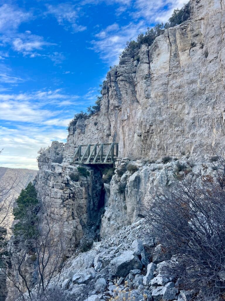 Wide view of wooden bridge built into limestone cliffs on the Guadalupe Peak Trail in Guadalupe Mountains National Park.