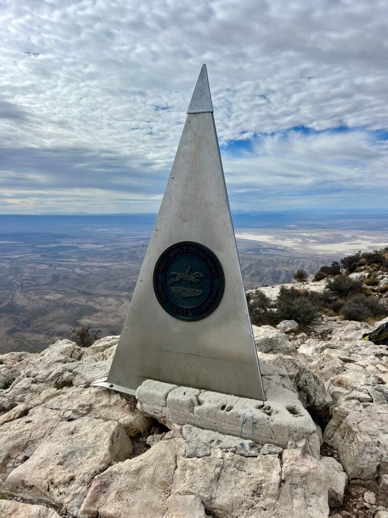 Stainless steel Guadalupe Peak summit monument overlooking West Texas desert landscape