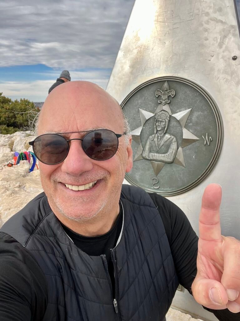 Smiling hiker taking a summit selfie beside the Guadalupe Peak monument