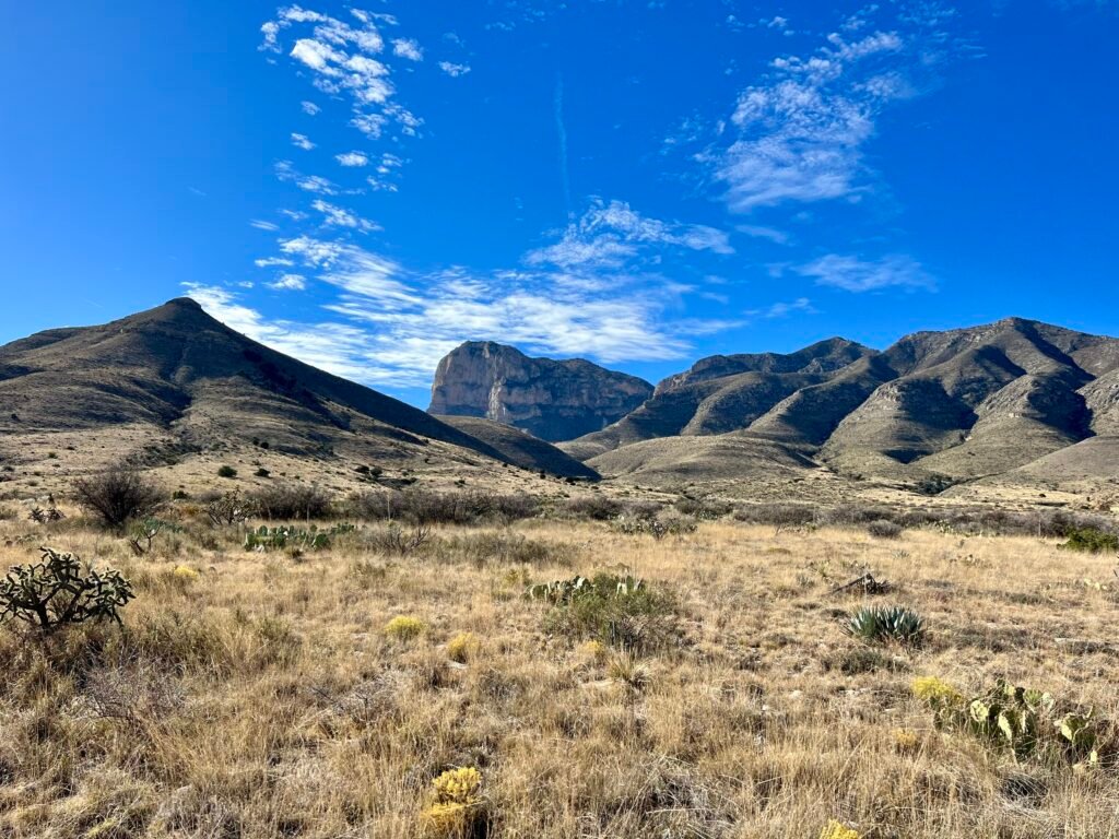 Side view of El Capitan rising above desert grasslands and rolling hills under a bright blue sky