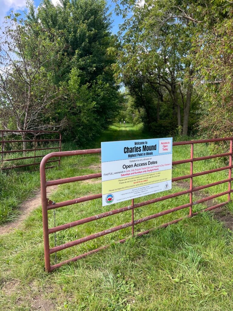 Farm gate entrance to Charles Mound with access sign and grassy path leading toward the Illinois high point.