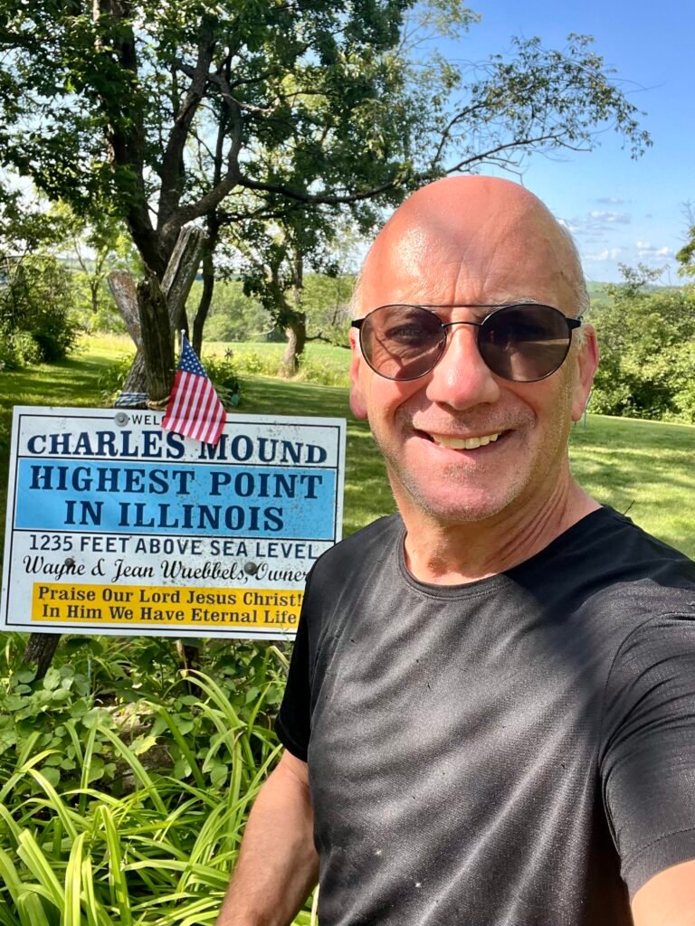 Smiling hiker at Charles Mound summit sign marking Illinois’ highest point at 1,235 feet.