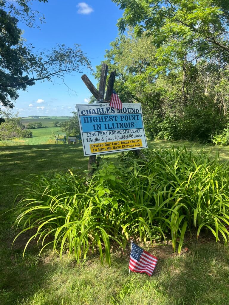 Charles Mound highest point sign with American flag and farmland views in Illinois.
