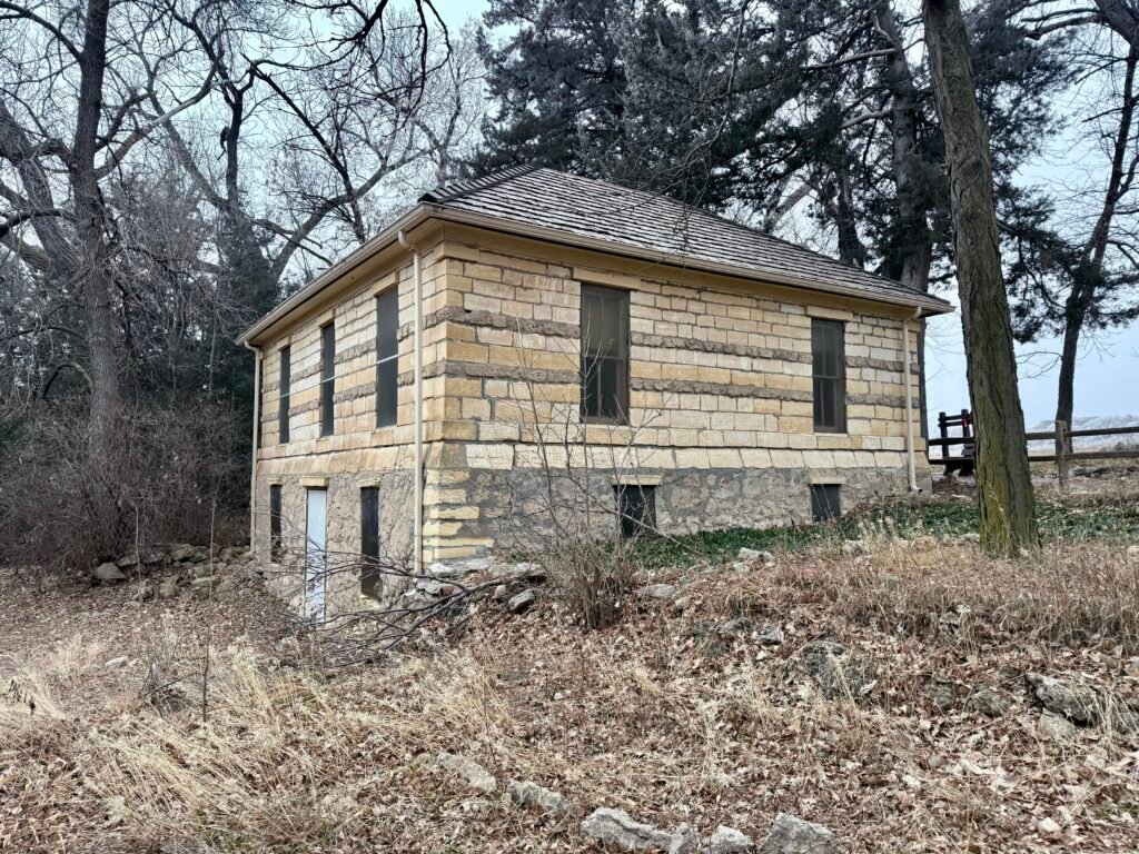 Rear view of the Steele Home Museum at Historic Lake Scott State Park surrounded by winter trees and stone foundation.