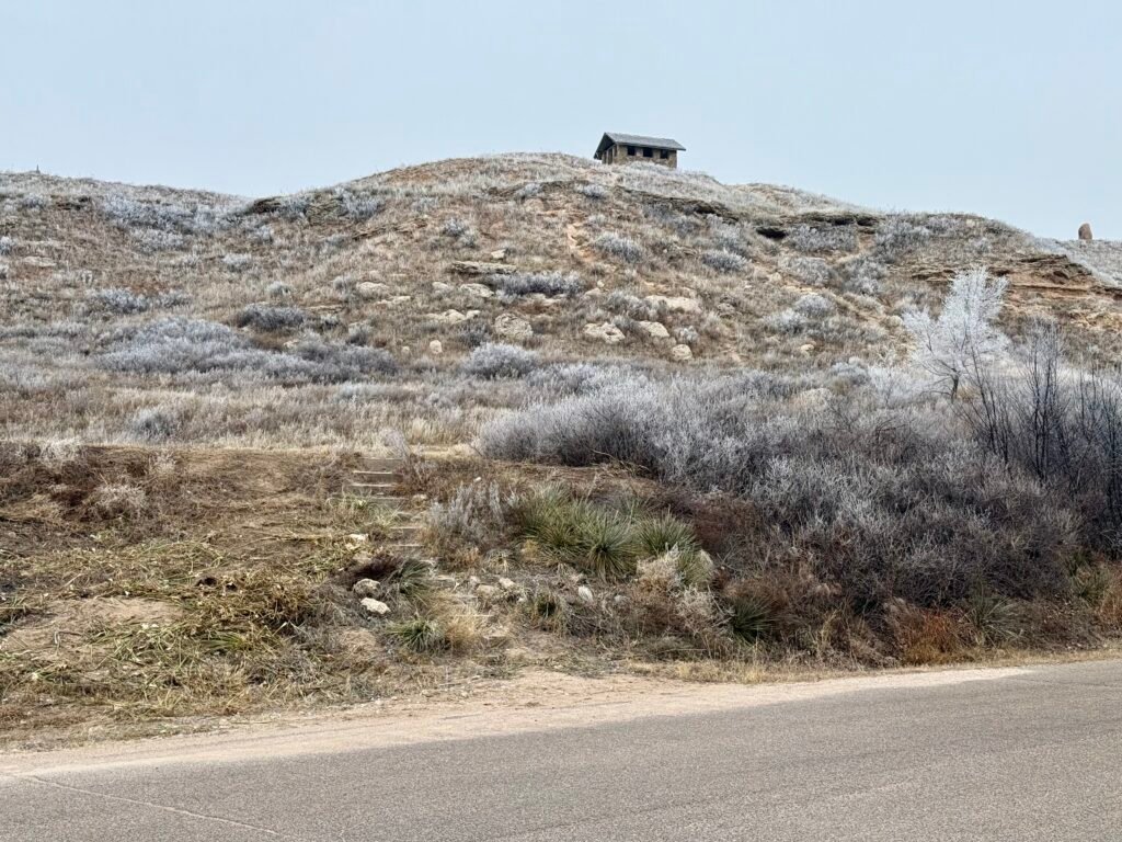 Trailhead at Historic Lake Scott State Park leading toward a small stone building on the bluff in winter.