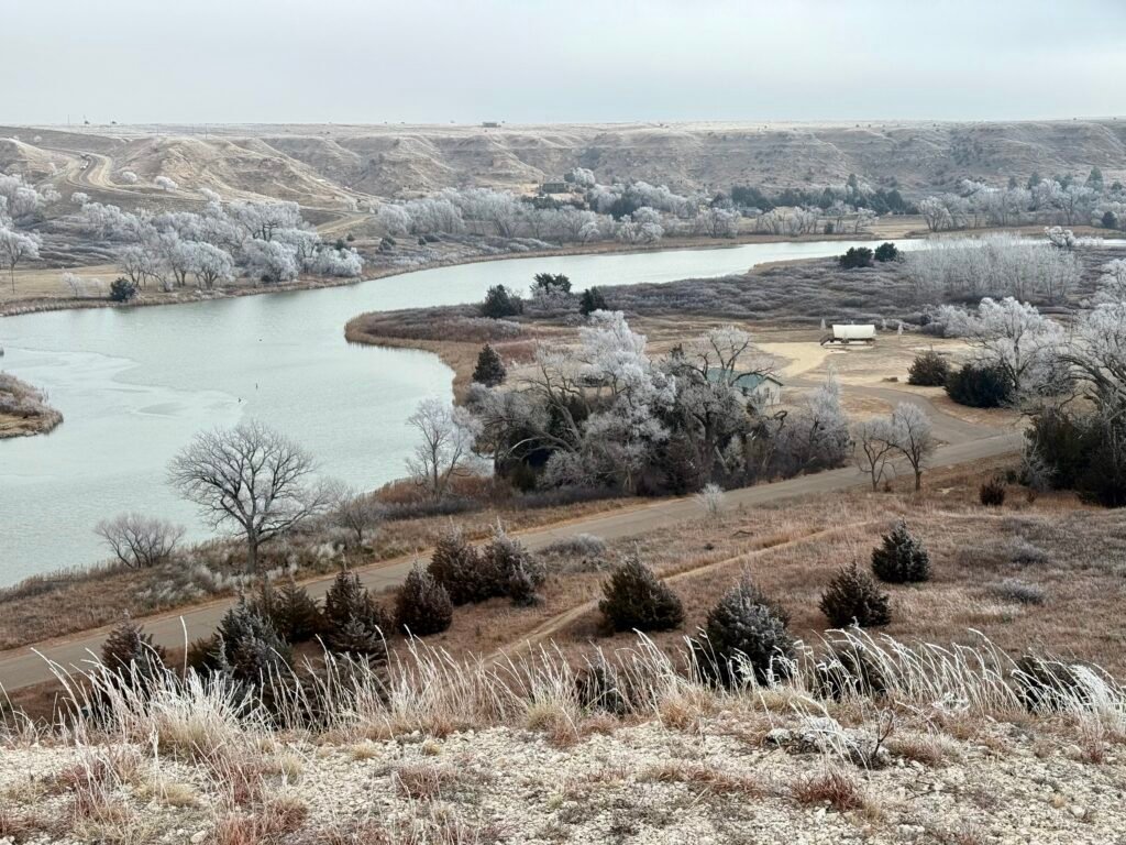 Overlook of Lake Scott with icy water and frost-covered cottonwood trees below Buzzard’s Point in winter.