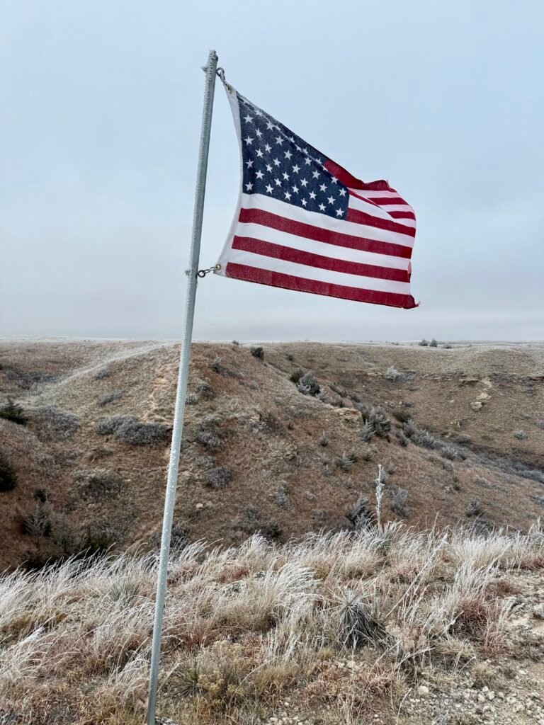 American flag waving on a frost-covered bluff overlooking the rolling hills and lake at Historic Lake Scott State Park.