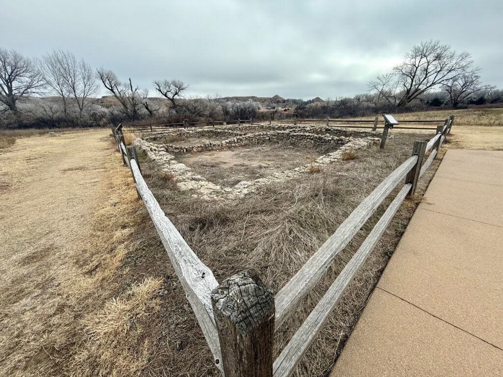 Stone foundation walls of the El Cuartelejo Pueblo ruins surrounded by a wooden fence in western Kansas.