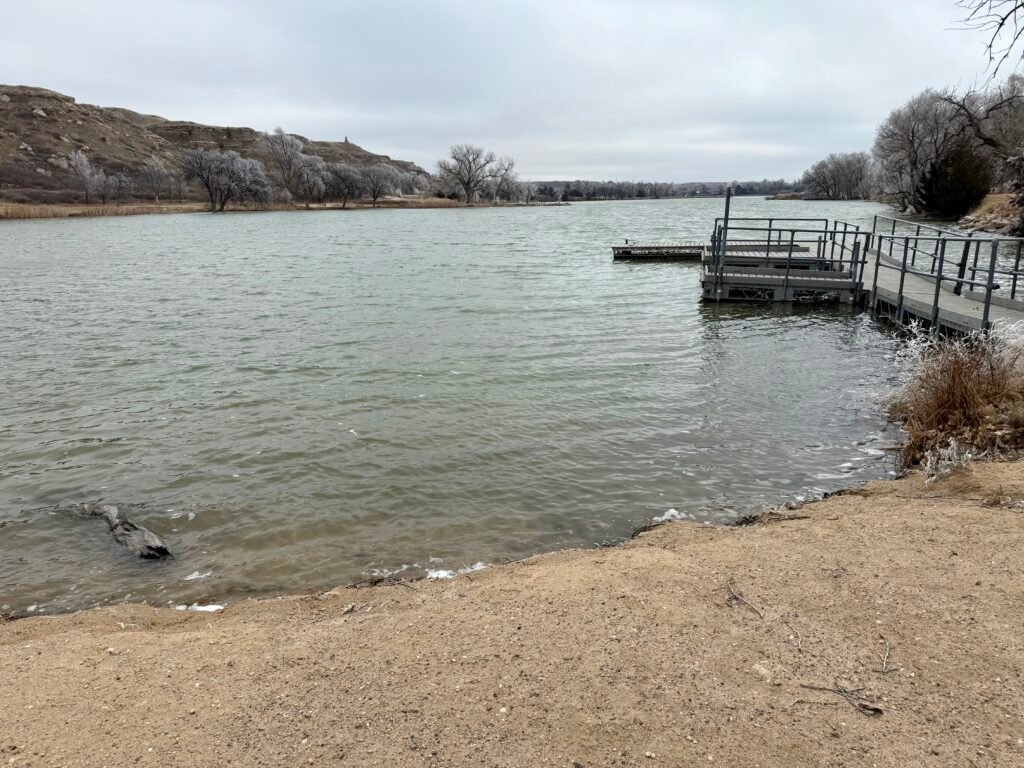 Choppy waters of Lake Scott beside a sandy shoreline and small dock, with frost-covered trees and overcast skies.