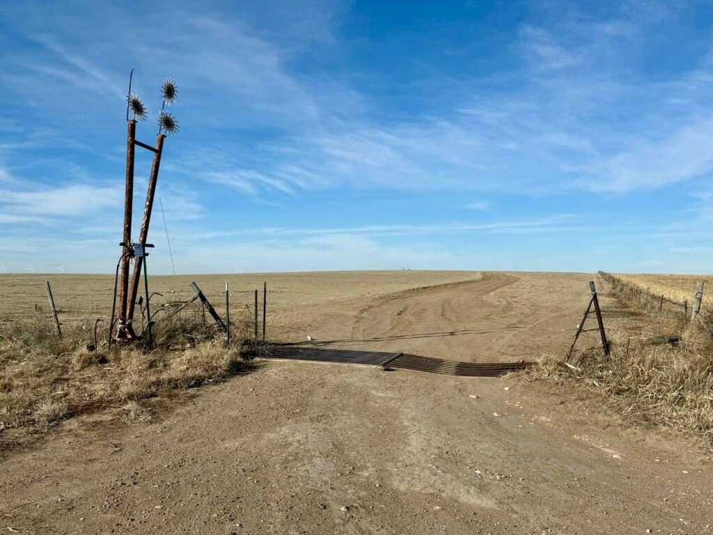 Dirt road and cattle guard leading to Mount Sunflower across the open Kansas High Plains under a clear sky.