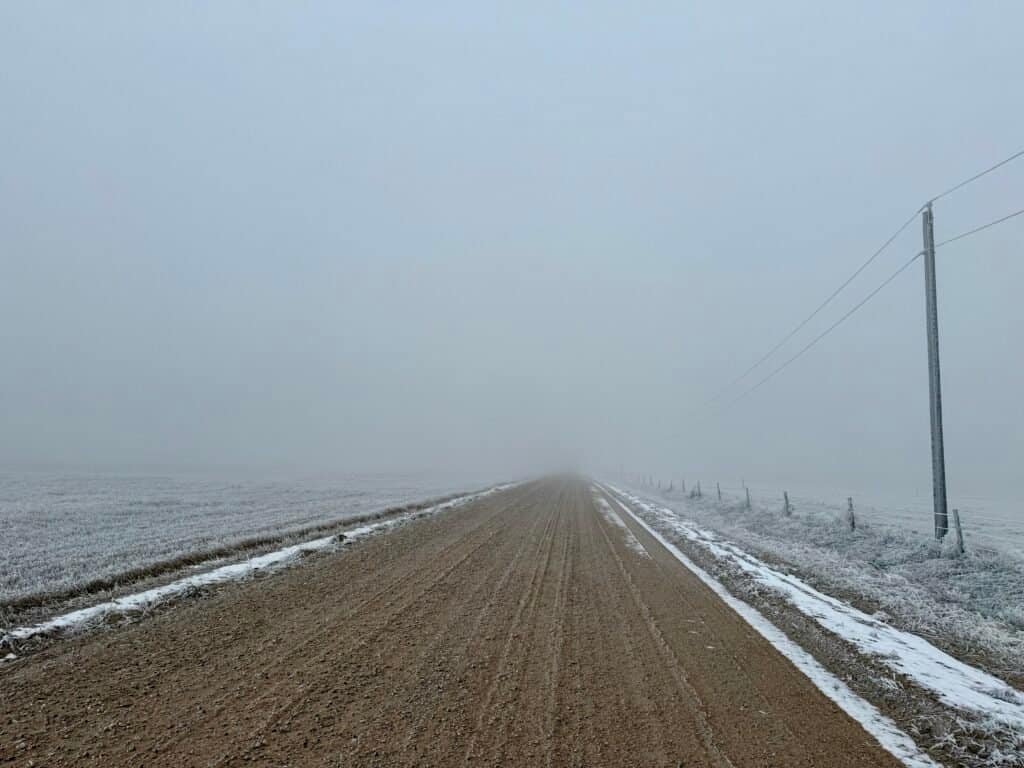 Fog-covered dirt road leading toward Panorama Point, Nebraska, with frost-lined fields and fence posts fading into the distance.