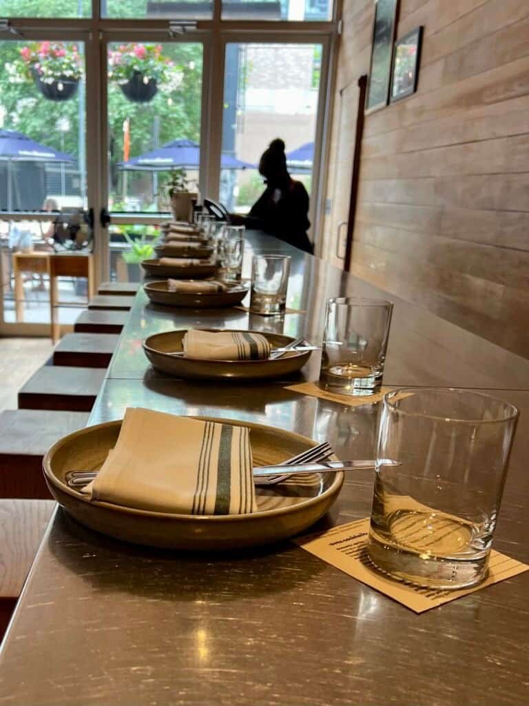 Place settings lined along the bar at avec with natural light and warm wood interior
