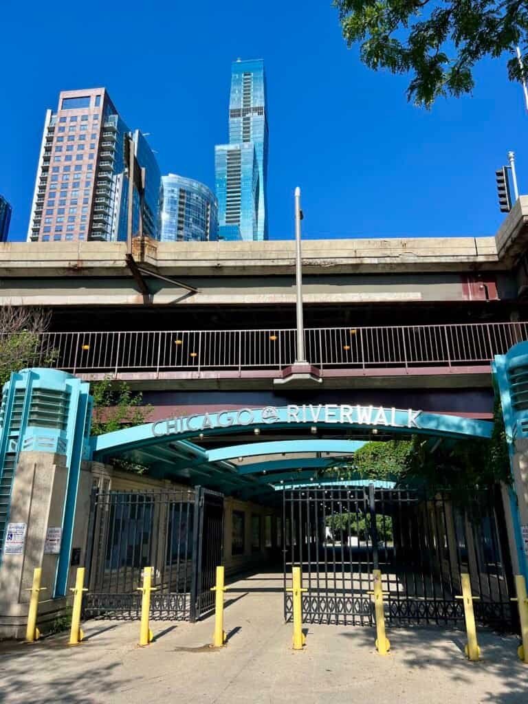 Entrance to the Chicago Riverwalk with downtown buildings rising above on a clear summer day