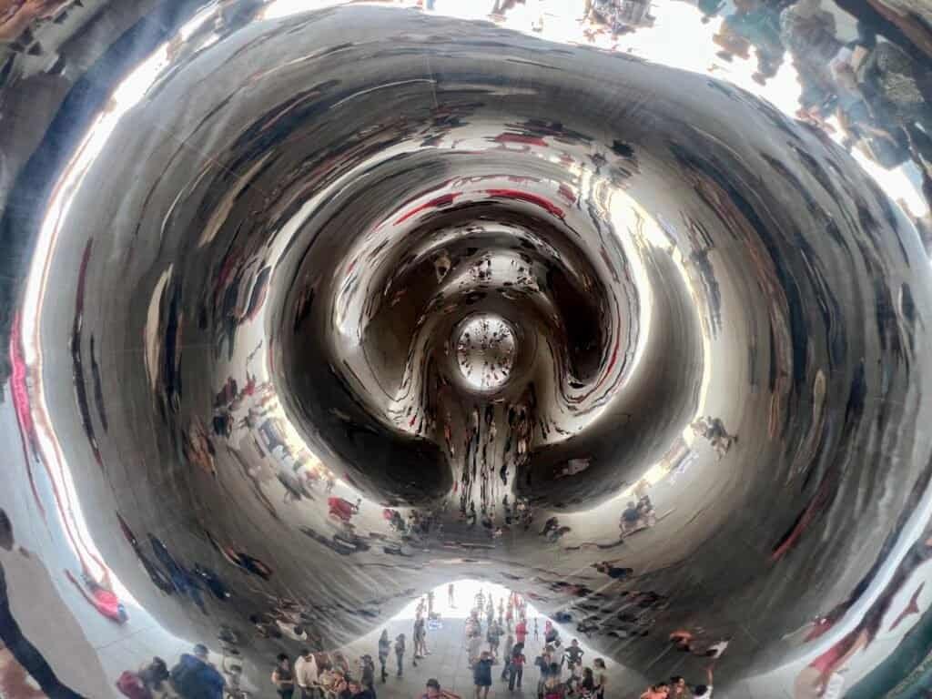 Distorted reflections of visitors beneath Cloud Gate inside the mirrored underpass in Millennium Park