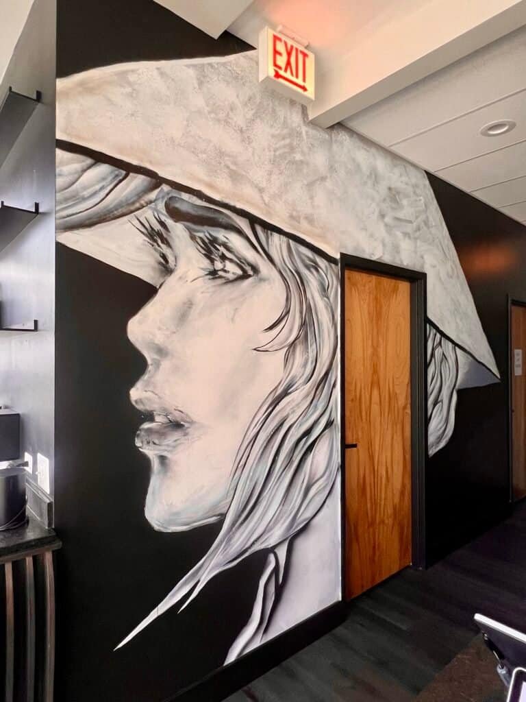 Black-and-white mural inside Fat Miilk Chicago featuring a woman in a wide-brim hat