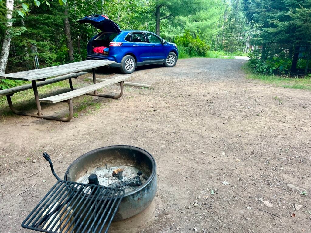 Campsite with picnic table, fire ring, and blue SUV at Tettegouche State Park.
