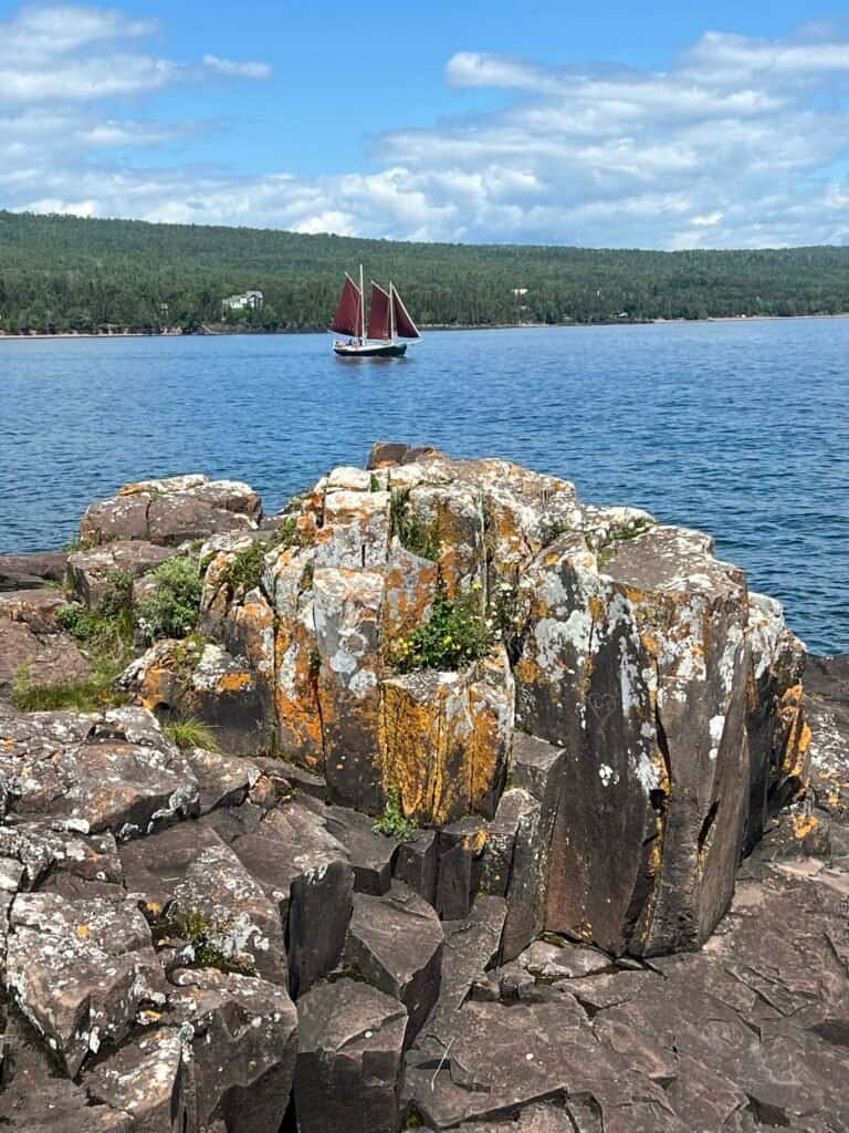 Basalt rock formations at Artist Point with a red-sailed schooner passing on Lake Superior near Grand Marais, Minnesota.
