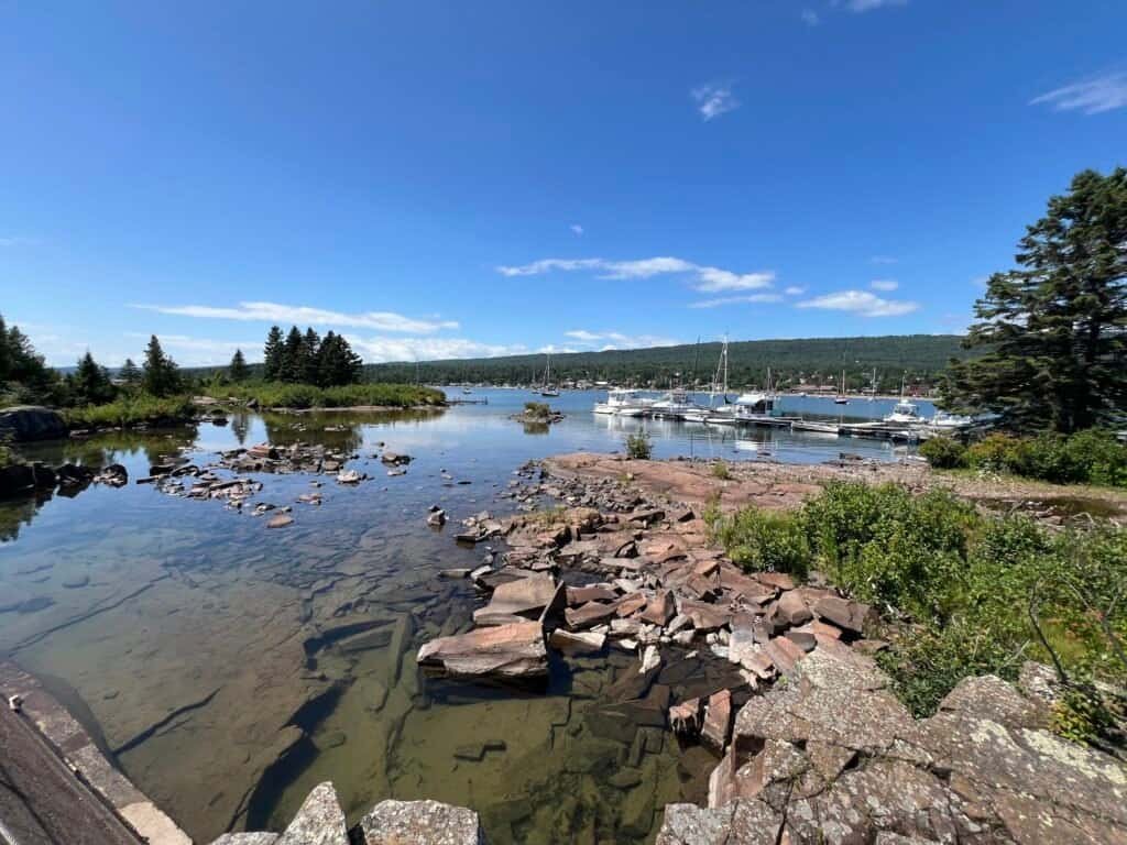 Calm harbor waters in Grand Marais with rocky shoreline, marina boats, and forested hills in the background
