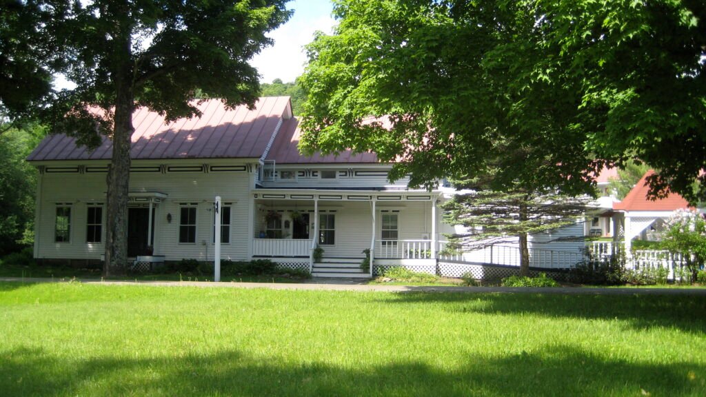 White farmhouse-style building with a red metal roof at Hostel Tevere in Vermont.