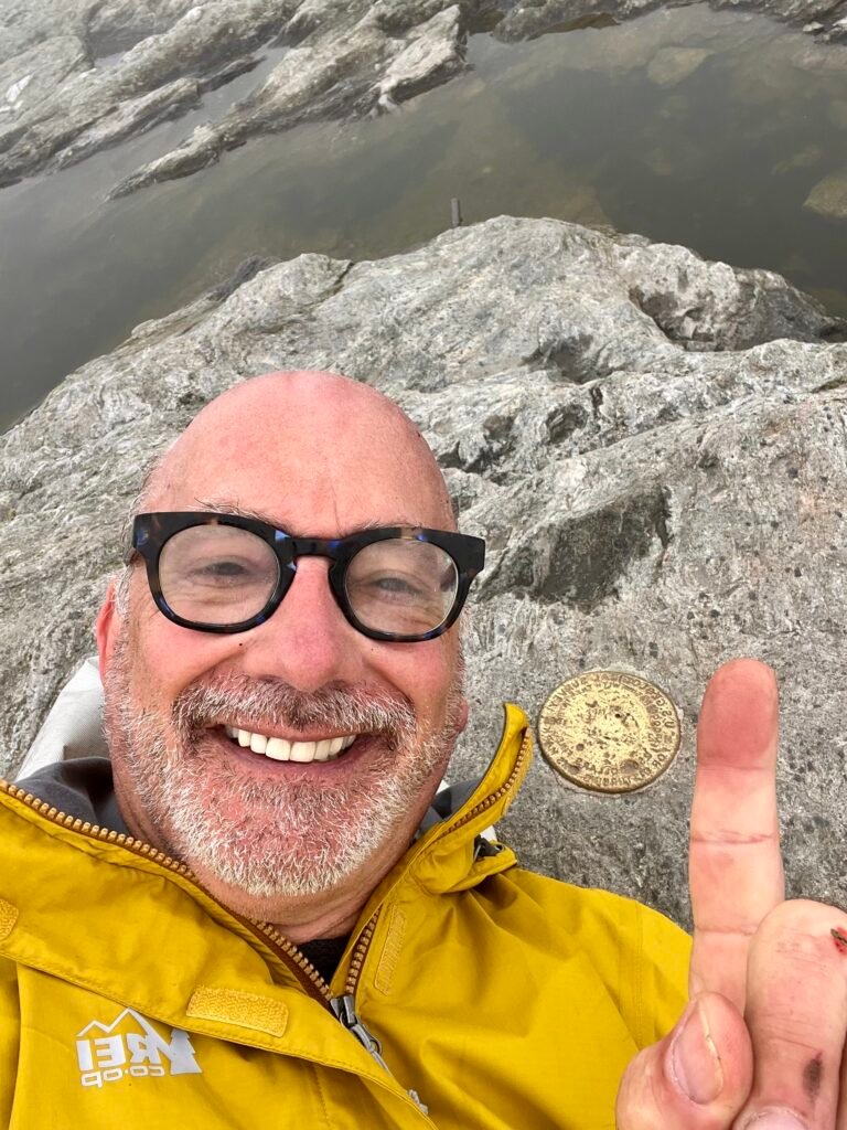Hiker pointing to the USGS summit marker on Mount Mansfield in foggy conditions.