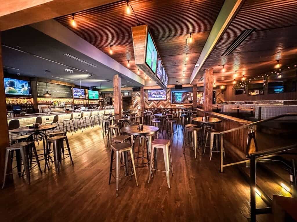 Wide view of Barstool River North interior with high-top tables, bar seating, and TVs.