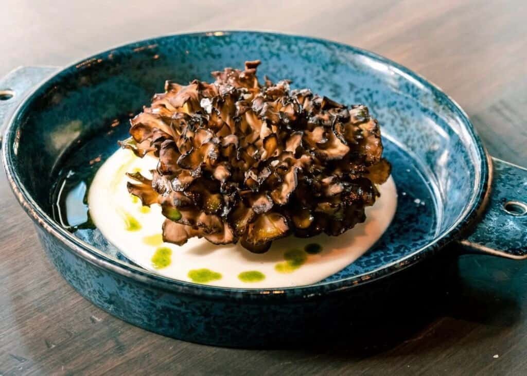 Roasted hen of the woods mushrooms plated over creamy sauce in a blue ceramic dish