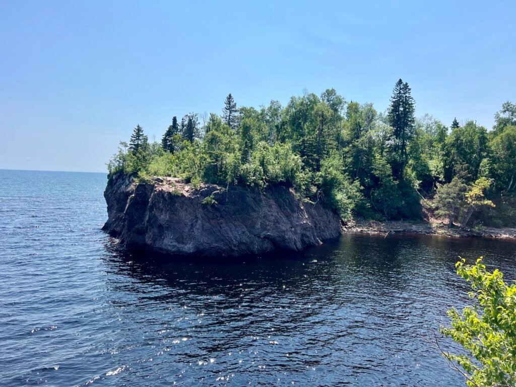 Forested rocky outcrop jutting into Lake Superior under clear blue skies.