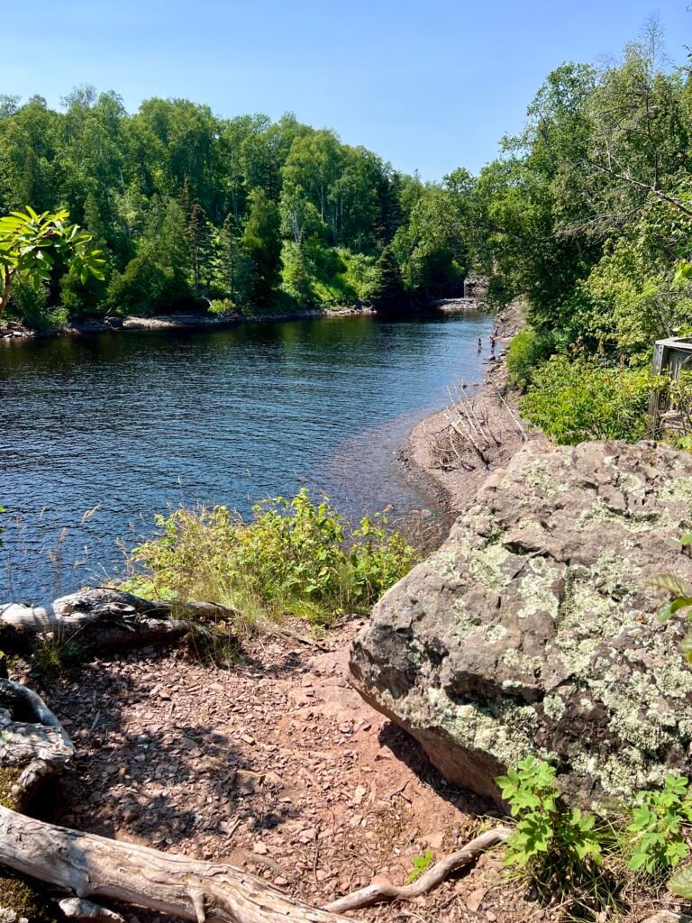 Calm stretch of the Baptism River surrounded by green forest on a sunny day.