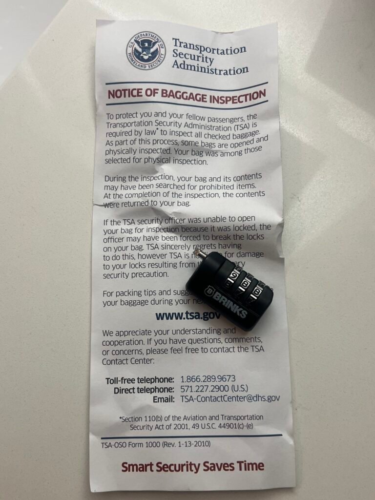 TSA Notice of Baggage Inspection slip with broken combination luggage lock placed on top.